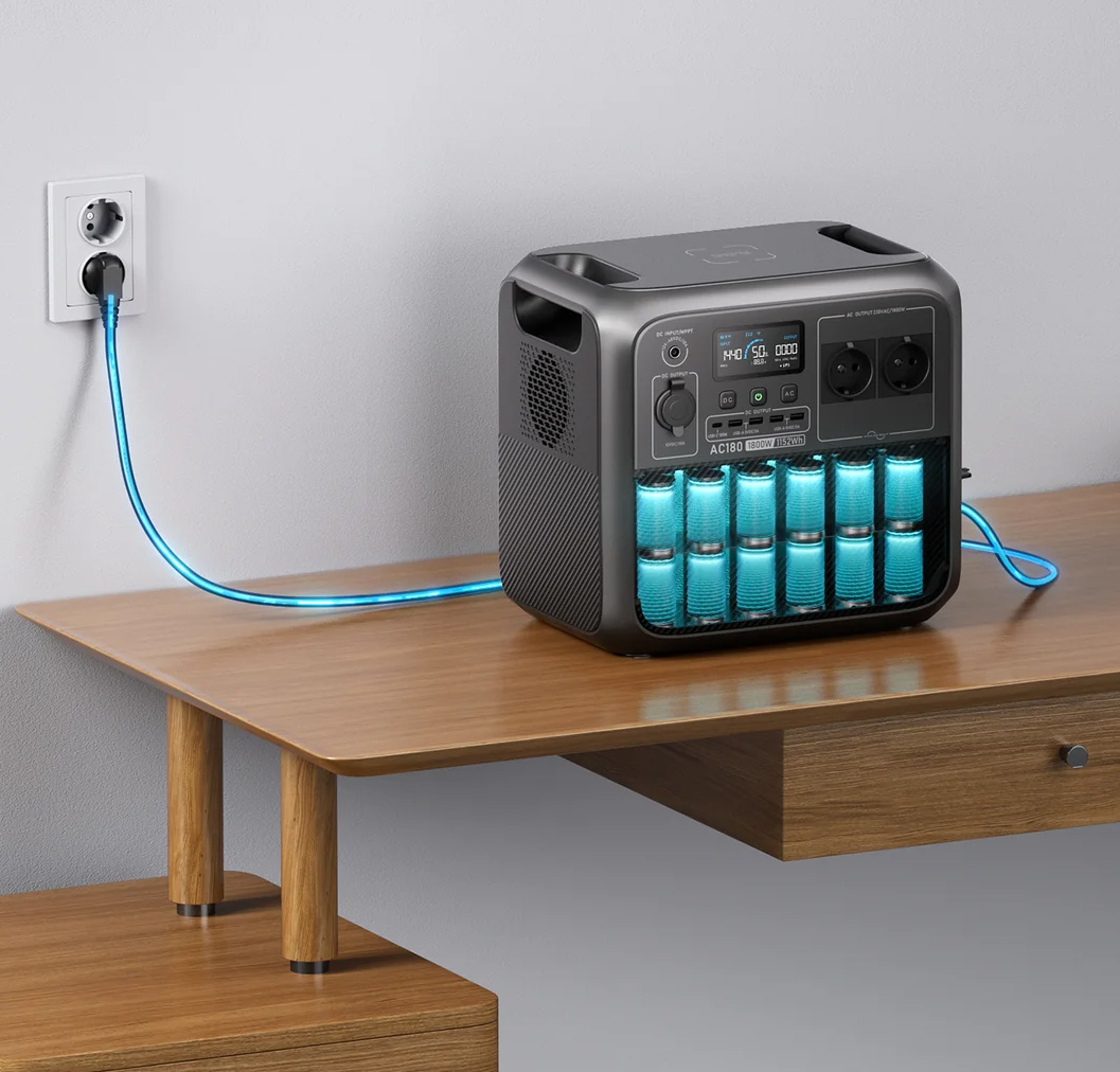 portable powerstation AC180 zwart met blauw verlichte batterij-indicatoren op houten tafel, aangesloten op wandcontactdoos met blauwe voedingskabel