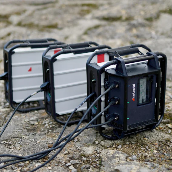 portable powerstation Instagrid met zwarte beschermbehuizing en display, gekoppeld via kabels aan twee identieke draagbare zonne-energie batterijen op rotsachtig terrein