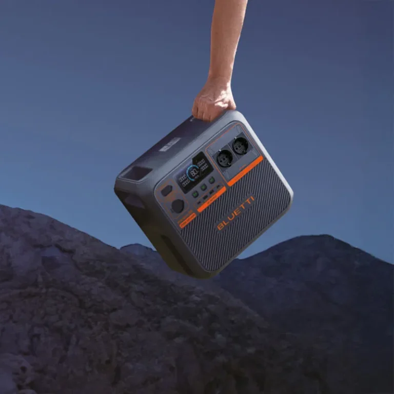 portable powerstation Bluetti EB3A in donkergrijs met oranje details, zichtbaar bedieningspaneel met display en stopcontacten, gehouden door hand tegen achtergrond van avondelijke rotsen