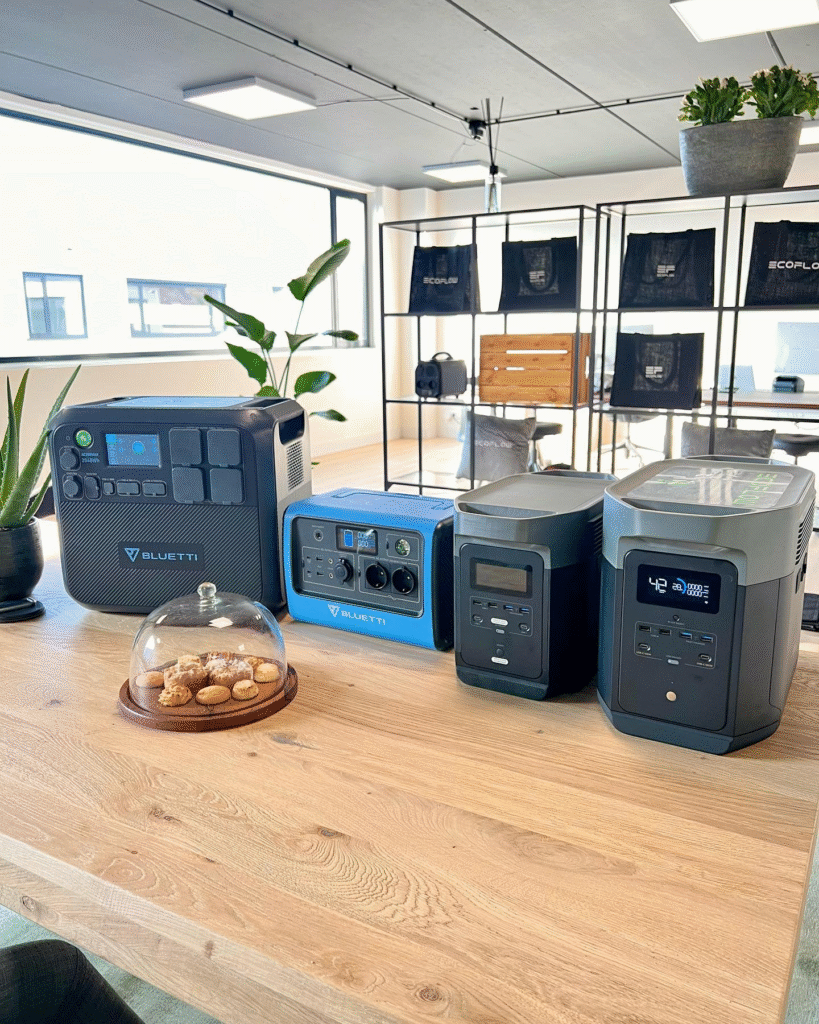 portable powerstations vier stuks op houten tafel in kantoorruimte met grote ramen en planten, inclusief zwarte en blauwe Bluetti modellen met digitale display en schakelaars