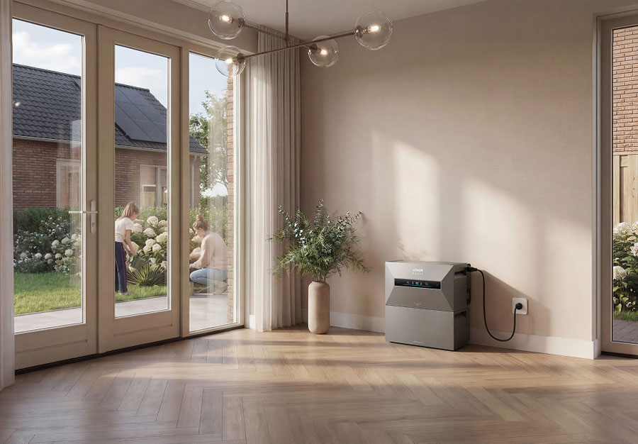 thuisbatterij grijs model van OffgridPowerStation.nl in lichte woonkamer naast glazen schuifdeur met tuin en mensen die buiten planten verzorgen