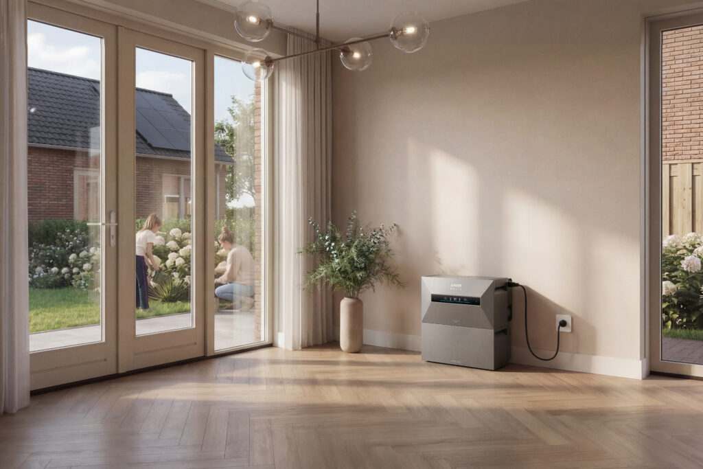 thuisbatterij Anker Solix grijs in moderne woonkamer bij licht houten vloer, met zonnepanelen zichtbaar op dak buiten en mensen in tuin op achtergrond